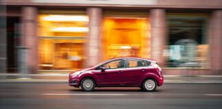 Czerwony Peugeot 207 jedzie szybko po miejskiej ulicy