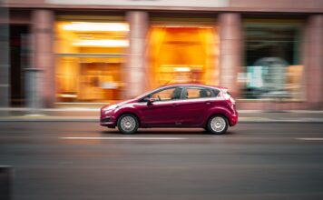 Czerwony Peugeot 207 jedzie szybko po miejskiej ulicy