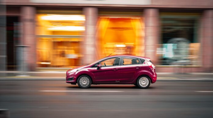 Czerwony Peugeot 207 jedzie szybko po miejskiej ulicy