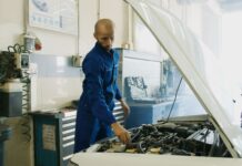 Mechanik w niebieskim kombinezonie sprawdza silnik benzynowy Peugeot w warsztaci