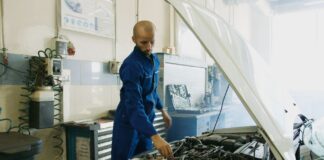 Mechanik w niebieskim kombinezonie sprawdza silnik benzynowy Peugeot w warsztaci