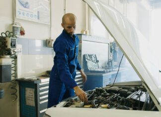 Mechanik w niebieskim kombinezonie sprawdza silnik benzynowy Peugeot w warsztaci