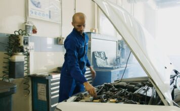 Mechanik w niebieskim kombinezonie sprawdza silnik benzynowy Peugeot w warsztaci