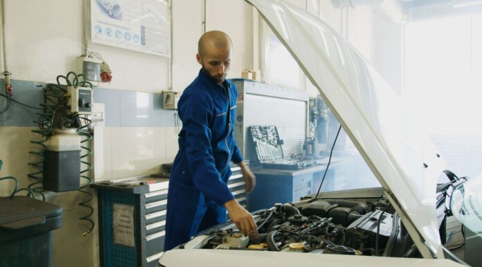 Mechanik w niebieskim kombinezonie sprawdza silnik benzynowy Peugeot w warsztaci