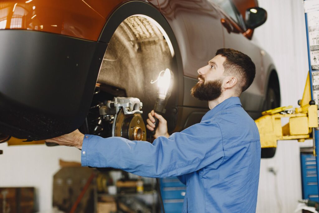Mechanik w niebieskim kombinezonie sprawdza hamulce samochodu w garażu
