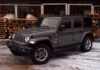 Szary Jeep Wrangler zaparkowany na śniegu wśród drewnian