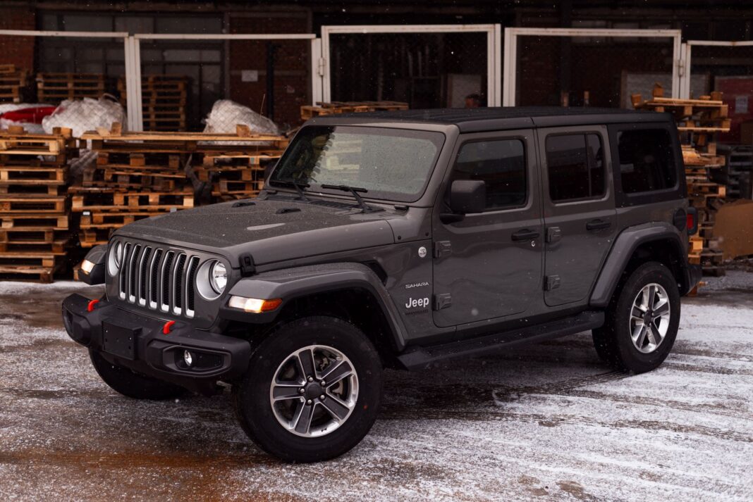 Szary Jeep Wrangler zaparkowany na śniegu wśród drewnian Szary Jeep Wrangler zaparkowany na śniegu wśród drewnian