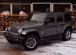 Szary Jeep Wrangler zaparkowany na śniegu wśród drewnian
